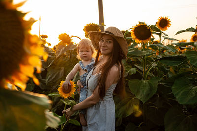 Beautiful mother holds a little son in her arms in a field of sunflowers at sunset