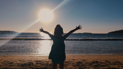 Woman standing at beach against sky during sunset