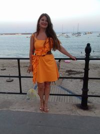 Young woman standing by railing against sea