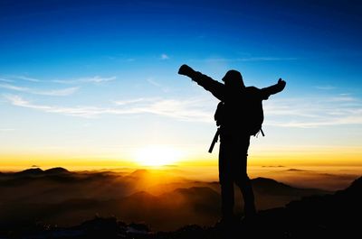 Silhouette of hiker on top of mountain at sunset