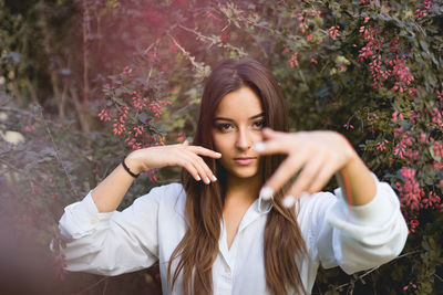 Portrait of young woman showing painted fingernails against plants