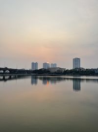 Reflection of buildings in city against sky during sunset