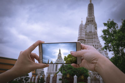 Cropped image of man photographing temple against sky