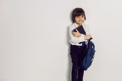 Child boy with a book textbook and backpack stands on a white background