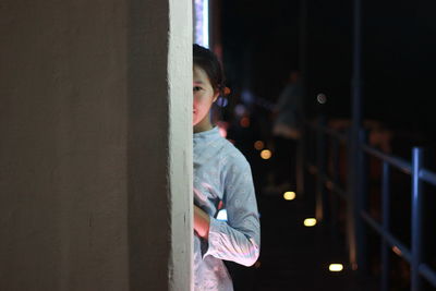 Portrait of woman standing by wall at night