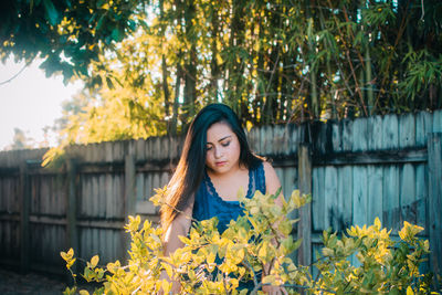 Young woman standing by plants against wooden fence