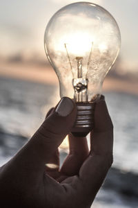 Close-up of hand holding light bulb against sky
