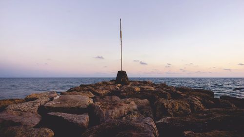 Lighting equipment on rock formation at sea against sky during sunset