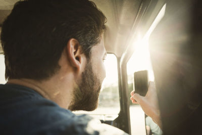 Rear view of man photographing through smart phone in car