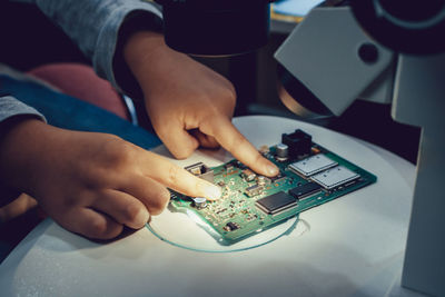 Cropped image of technician adjusting circuit board on microscope slide indoors