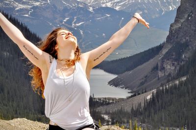 Happy beautiful woman with arms raised standing against mountains