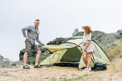 Happy young couple travelers in casual outfits near tent in mountains. local tourism, weekend 