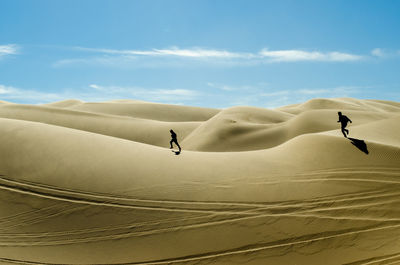 Two people running on sand dune in desert