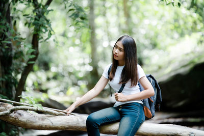 Young woman sitting on tree against plants