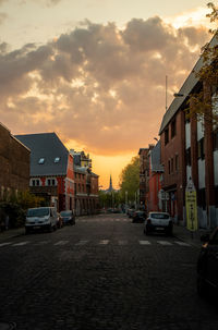 Cars on road by buildings against sky during sunset