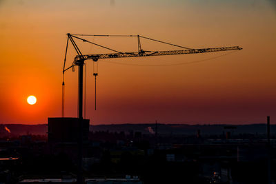 Silhouette cranes at construction site during sunset