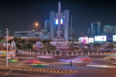 Illuminated city street by buildings against sky at night