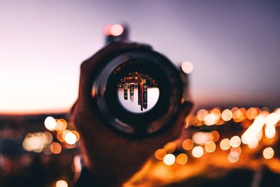 Cropped hand of person photographing of illuminated buildings against clear sky during dusk