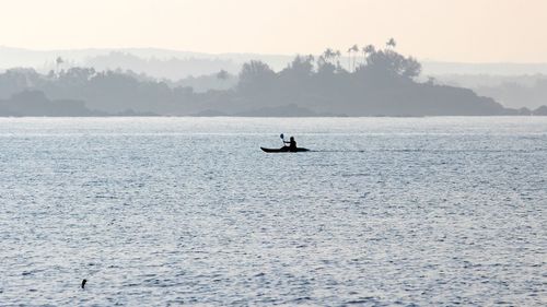 Silhouette man on boat in sea against sky