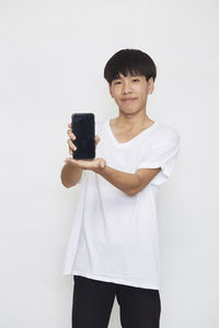Portrait of man holding camera while standing against white background