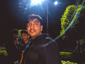 Portrait of smiling man standing against illuminated wall at night