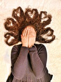 High angle view of woman with hands covering face lying on bed