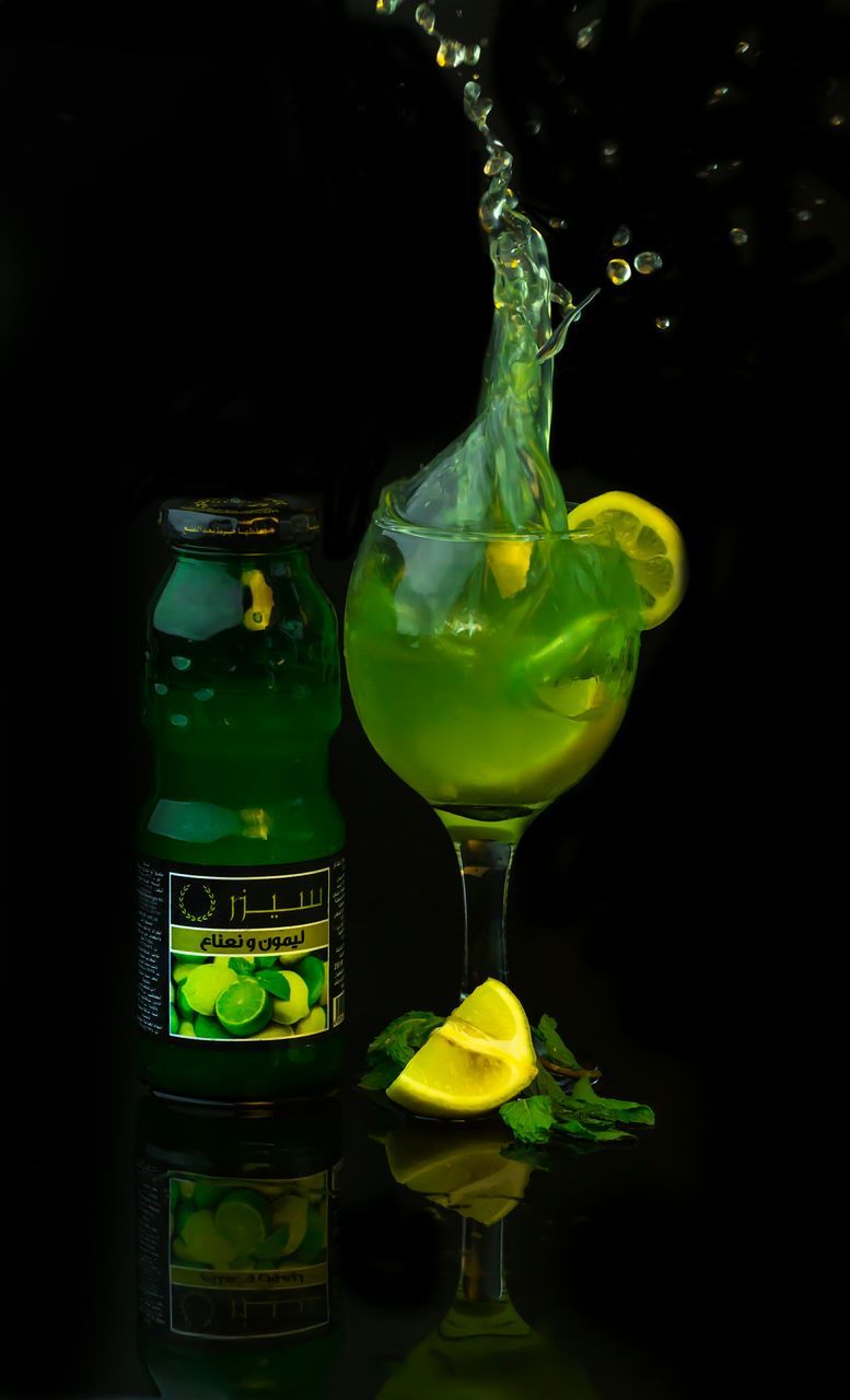 glass - material, close-up, transparent, indoors, studio shot, illuminated, focus on foreground, black background, still life, glass, drinking glass, green color, yellow, refreshment, night, drink, human representation, reflection, no people, bottle