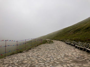 Footpath leading towards mountains against clear sky