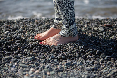Low section of woman standing on pebbles at beach