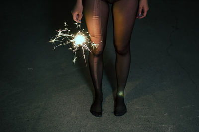 Low section of woman with sparkler standing on walkway at night
