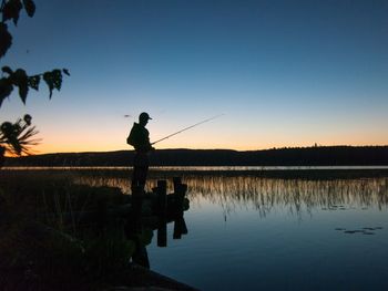 Silhouette man fishing on lake against sky during sunset