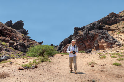 Man with camera walking against rock formation and sky