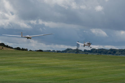 Airplane flying over grassy field against sky