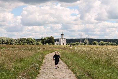 Rear view of man walking on field against sky