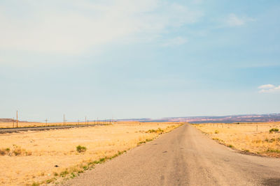 Dirt road amidst field against sky