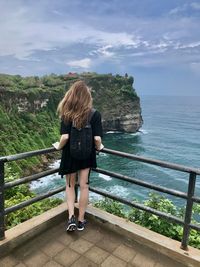 Rear view of woman standing by railing against sea