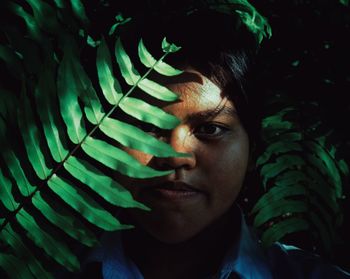 Close-up portrait of young woman standing by plant leaves