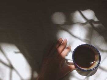 Cropped hand of person with coffee on bed at home