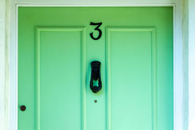 House number 3 in black iron on a mint green wooden front door in london