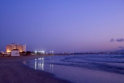 Illuminated buildings by sea against sky at night