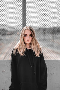 Portrait of beautiful young woman standing against fence