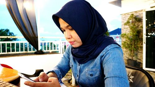 Woman wearing hijab using phone while sitting on chair