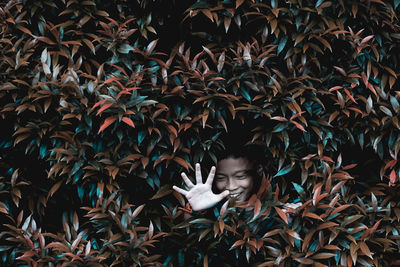 Happy boy showing stop gesture amidst plants leaves