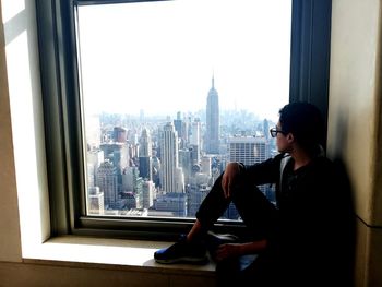 Teenage boy looking at city buildings seen through glass window