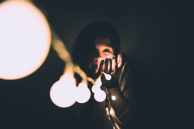 Portrait of young woman holding illuminated string lights in darkroom