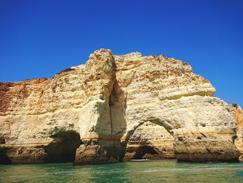 Rock formation by sea against clear blue sky