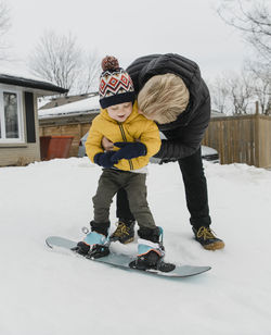 Loving father embracing son learning snowboarding during winter