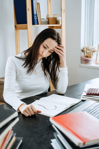 Female accountant looking to question mark in a notepad on the background of laptop and calculator