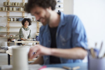 Portrait of smiling woman learning pottery while man in foreground at art studio