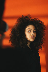 Portrait of woman standing against orange curtain